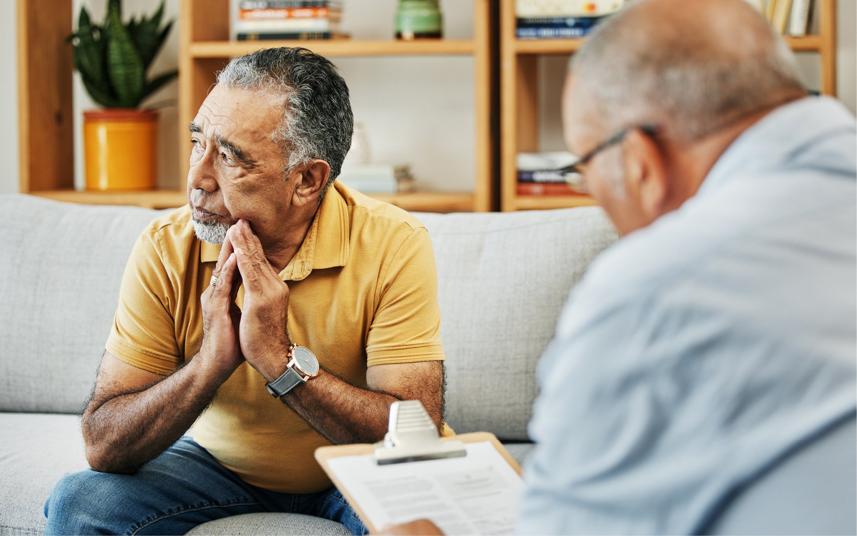 older man sitting on a couch talking to another man with a clipboard